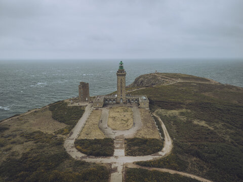Aerial view of the stark Cap Fr&Atilde;&copy;hel lighthouse piercing the grey sky, standing resolute against the turbulent sea, a beacon of hope against the dramatic cliffs, Pl&Atilde;&copy;venon, Bretagne, France.