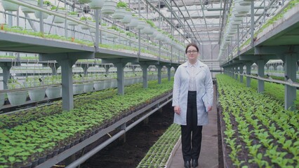 Smiling woman ecologist walking through greenhouse, inspecting plant growth