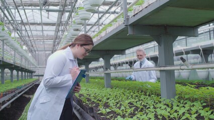 Experts analyzing plant growth in greenhouse, documenting findings for research