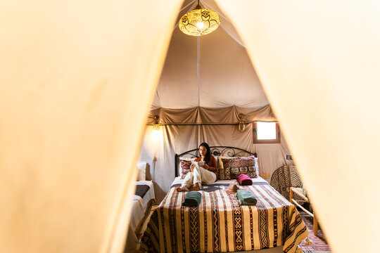 Woman reading in cozy glamping tent with boho decor in Morocco desert