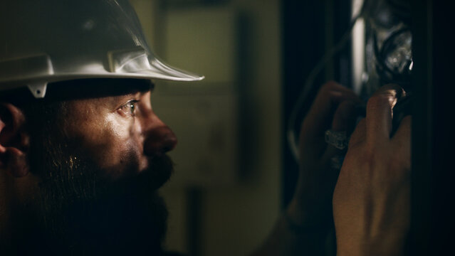 Man, technician and check wires in server room for inspection, electric maintenance and diagnostics. Male person, hardhat and database to repair cables, monitor system and circuit board for hardware - Powered by Adobe
