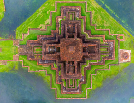 Aerial view of the ancient Somapura Mahavihara, a terracotta-hued monastery surrounded by tranquil waters and vibrant green vegetation, Naogaon, Somapura Mahavihara's, Bangladesh.