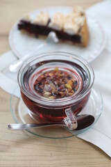 Glass of tea with a spoon in it sits on a table next to a slice of pie