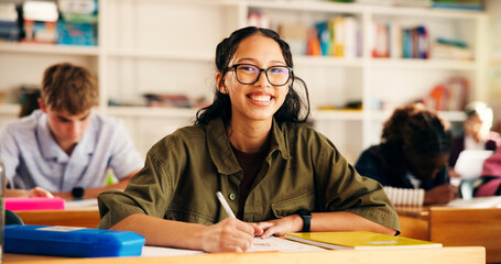 Education, classroom and happy teen writing in high school for test, learning or academic...