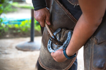 Close up farrier man using hammer nailing horseshoe hoof in stable