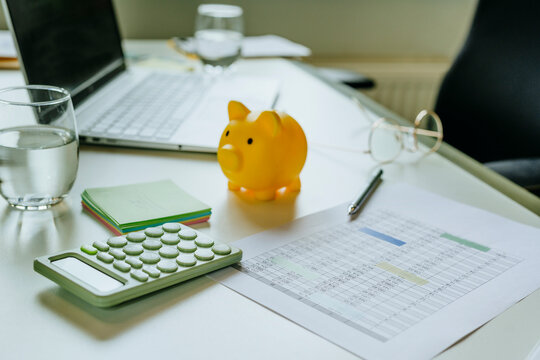 Yellow piggy bank and calculator on office desk with financial documents