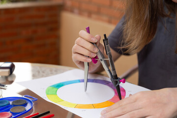 Young hands using a compass to draw a color wheel on paper. Outdoor setting with natural light. Visible art materials. Copy space. Concept of artistic technique and structured learning