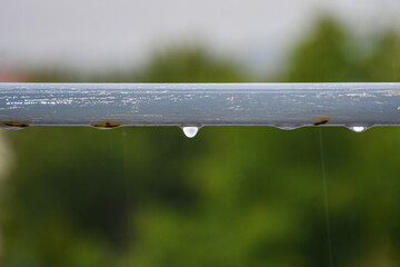 Gray handrail with water droplets and rust in a blurred forest background