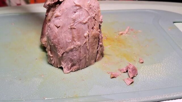 Chunks of cooked beef are being diced on a green cutting board using a sharp cleaver.