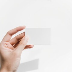 Fototapeta premium A hand holds a blank white business card against a plain white background.