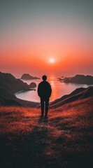 Obraz premium A silhouetted figure stands atop a grassy hill, gazing toward a radiant sunset over an ocean dotted with islands. The warm hues create a serene scene