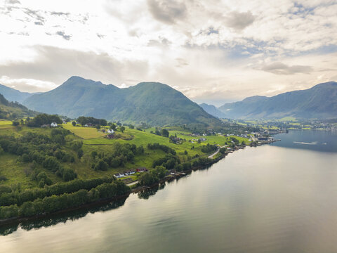 Aerial view of still, reflective waters mirroring the verdant slopes and distant peaks under a soft, diffused light, Hardanger fjord, Vestland, Norway.