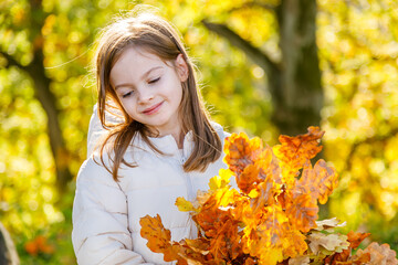 A sweet little girl looks down at a beautiful bouquet of golden oak leaves on a sunny autumn day