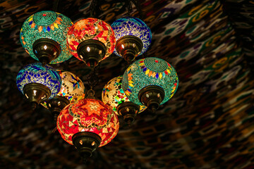 Ornate cluster of glowing Moroccan or Turkish mosaic lamps with colorful geometric patterns hanging...