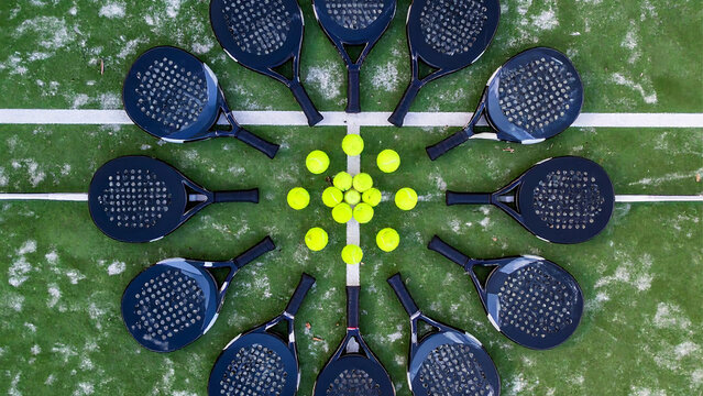 A top-down view of a sport padel tennis court with racquets arranged in a circle around a cluster of yellow balls