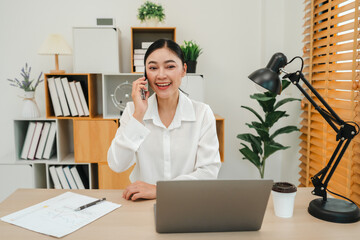 happy woman talking with smartphone while working with laptop computer at home office