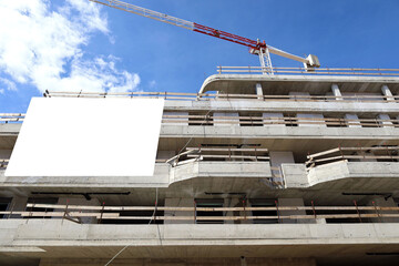 Blank information board on the facade of a new building under construction still in rough concrete . Tower crane and sky above. Background for copy space.
