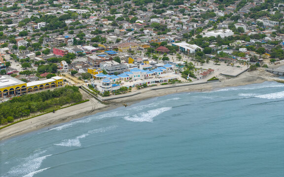Aerial view of turquoise waters meeting sandy shores, buildings painted in vivid blues and yellows nestled among lush greenery, Puerto Colombia, Atlantico, Colombia.