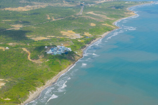 Aerial view of the coastline where the emerald sea meets the sandy shore near a cluster of buildings, Atlantico, Colombia.