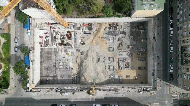 Aerial view construction site with a foundation pit of new skyscraper timelapse. Earthwork in excavation and backfilling of soil. Heavy machinery for earthmoving with crane, truck and bulldozer. 