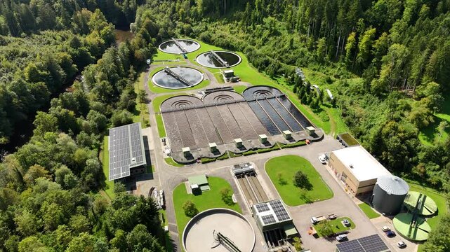 Aerial drone view of modern wastewater treatment facility with circular clarifier tanks processing sewage surrounded by green forest in Germany