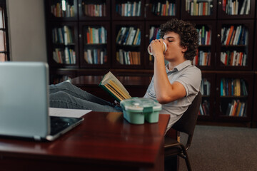Student drinking coffee and reading a book in the library
