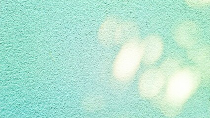 Abstract turquoise and pastel green wall with sunlight and shadow of tropical plants, creating a serene and natural aesthetic background.