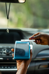 African woman making contactless credit card payment for transport fare using POS terminal inside a car.
