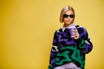 Stylish blonde woman poses confidently in trendy outfit against vibrant yellow backdrop