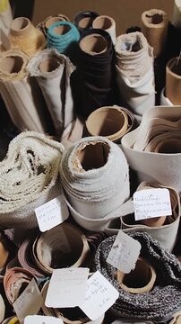 Vertical video. Rolls of fabric and textiles stacked on shelves in a furniture factory. Close-up of the warehouse, various fabrics, slow motion.