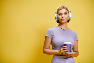Stylish blonde woman with headphones enjoying a coffee in a vibrant studio space