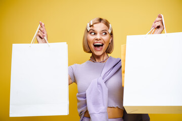 Trendy blonde woman showcases her stylish outfits with shopping bags in a vibrant studio