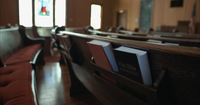 Close-up of wooden church pew with a Holy Bible and hymn book placed in the holder. The scene highlights faith, worship, and the sacred atmosphere of a traditional church interior.