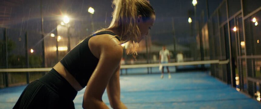 Female padel player serves during a competitive and intense match on a rainy night