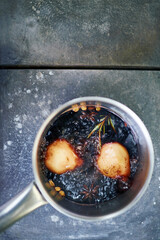 Top view showing saucepan containing two poached pears simmering in spiced red wine with visible star anise, cinnamon, and rosemary on rustic metal surface