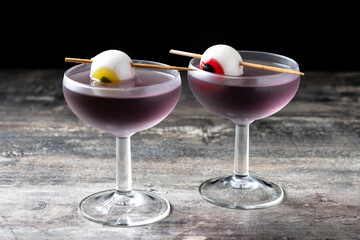 Purple Halloween cocktail garnished with candy eye on wooden table