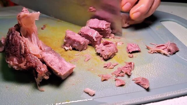 Sliced cooked beef on a green chopping board with a sharp kitchen cleaver.