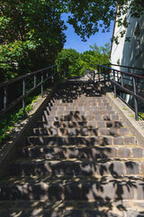 Outdoor stone staircase flanked by metal railings, leading upward through a green, leafy environment