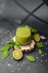 Green smoothie with basil, lime slices and spinach leaves on a dark stone surface with coarse salt.
