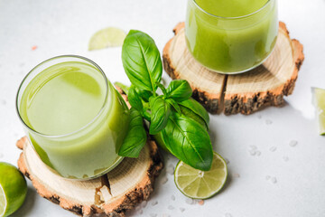 Two glasses of green healthy drink with fresh basil leaves and lime slices on wood rings.