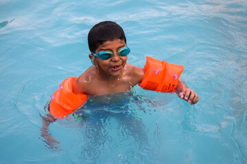 Happy Indian boy swimming in a pool, Kid wearing swimming costume along with air tube during hot...