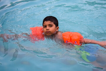 Happy Indian boy swimming in a pool, Kid wearing swimming costume along with air tube during hot...