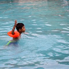 Happy Indian boy swimming in a pool, Kid wearing swimming costume along with air tube during hot...