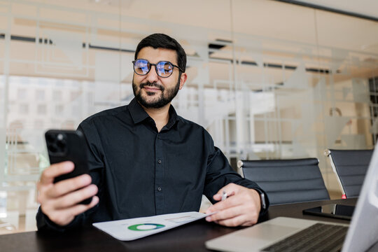 Professional man engaged in a digital meeting while reviewing data on his smartphone in a modern office setting
