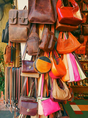 Leather bags, backpacks, shoes, sandals, and belts hang in dense, colorful street-side display in...