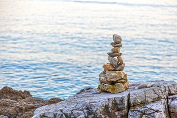 Balanced stone tower on seaside rocks. Stacked stones form a balanced tower on rugged coastal...