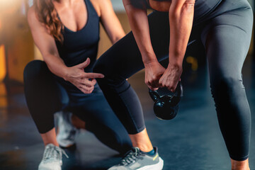 Using a kettle bell with a personal trainer, a mid adult woman improves power and flexibility in the gym. Customized workouts support health goals and enhance overall wellbeing.