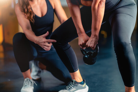 Using a kettle bell with a personal trainer, a mid adult woman improves power and flexibility in the gym. Customized workouts support health goals and enhance overall wellbeing.