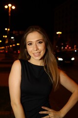 A young woman smiles while posing in a stylish black dress against a backdrop of a bustling city at...