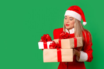 Smiling woman in Christmas attire holds colorful wrapped gifts against a green background during festive season